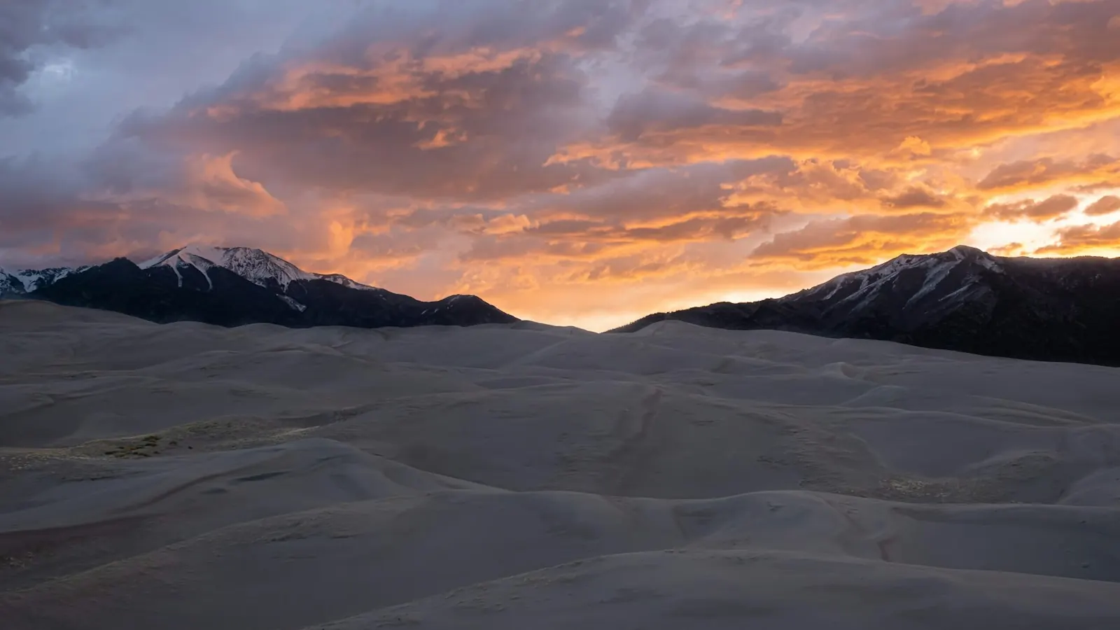 Sanft geschwungene Sanddünen vor schneebedeckten Bergen im Abendlicht